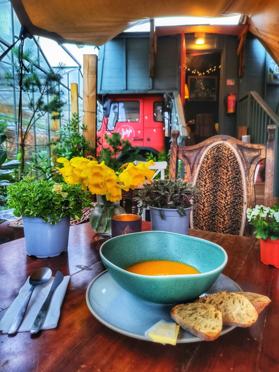 Soup and bread on a cafe table, daffodils beside it, the red Joly's truck beyond